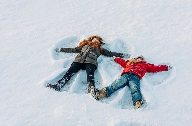 två barn ligger på marken i snö och gör snöänglar