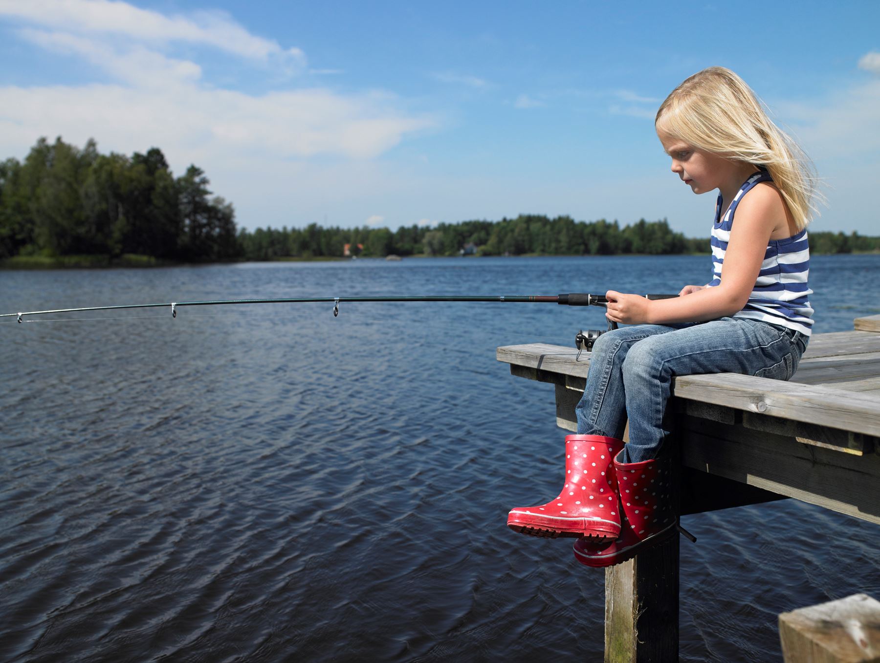 En ljushårig flicka som sitter på en bro och fiskar